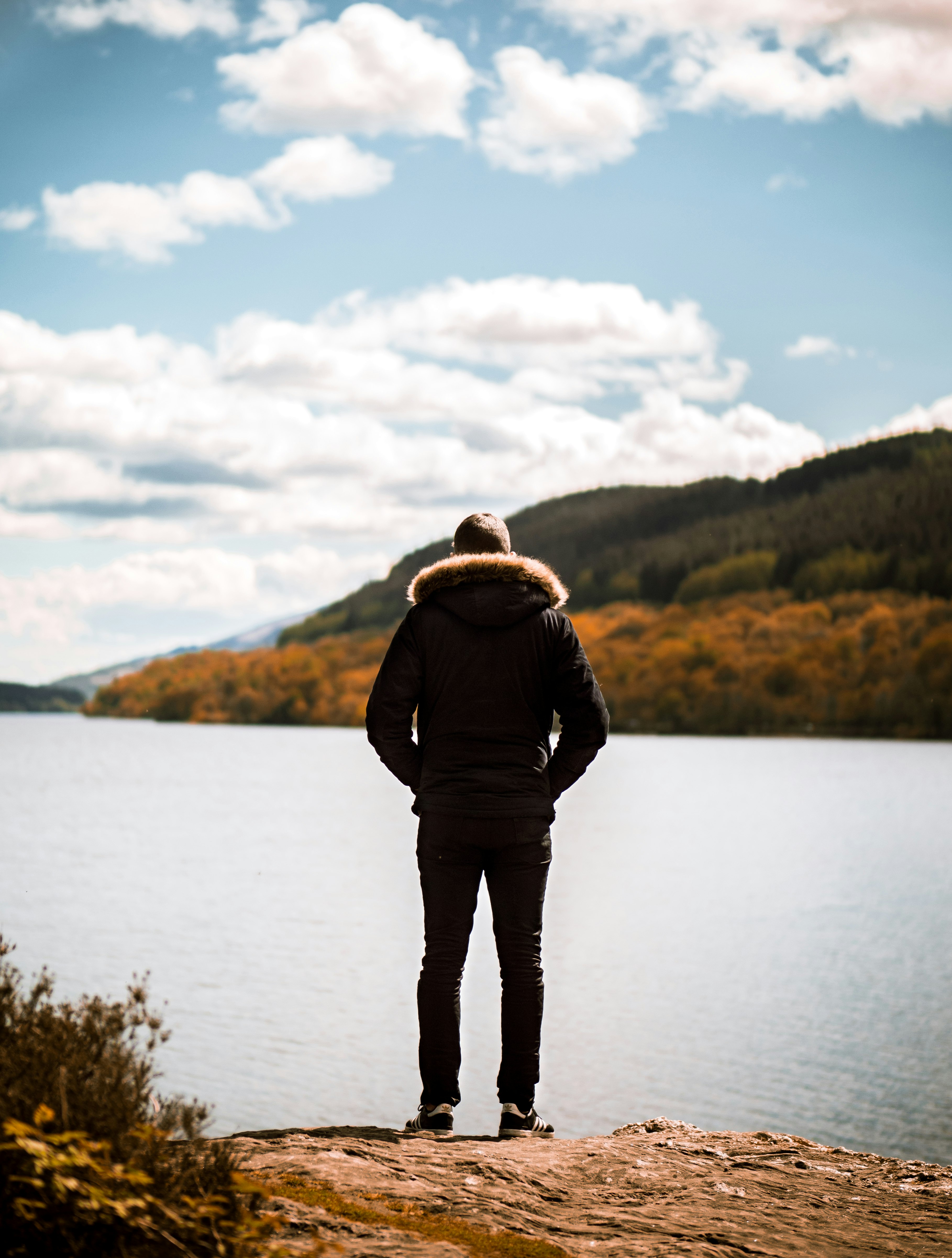 person wearing jacket standing on front of calm body of water during daytime